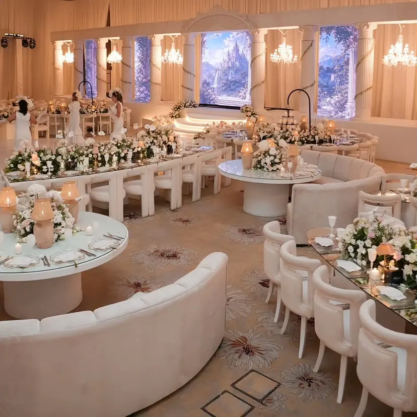 A wide view of the ballroom: long flower tables, cream sofas and the dance floor in front of the stage