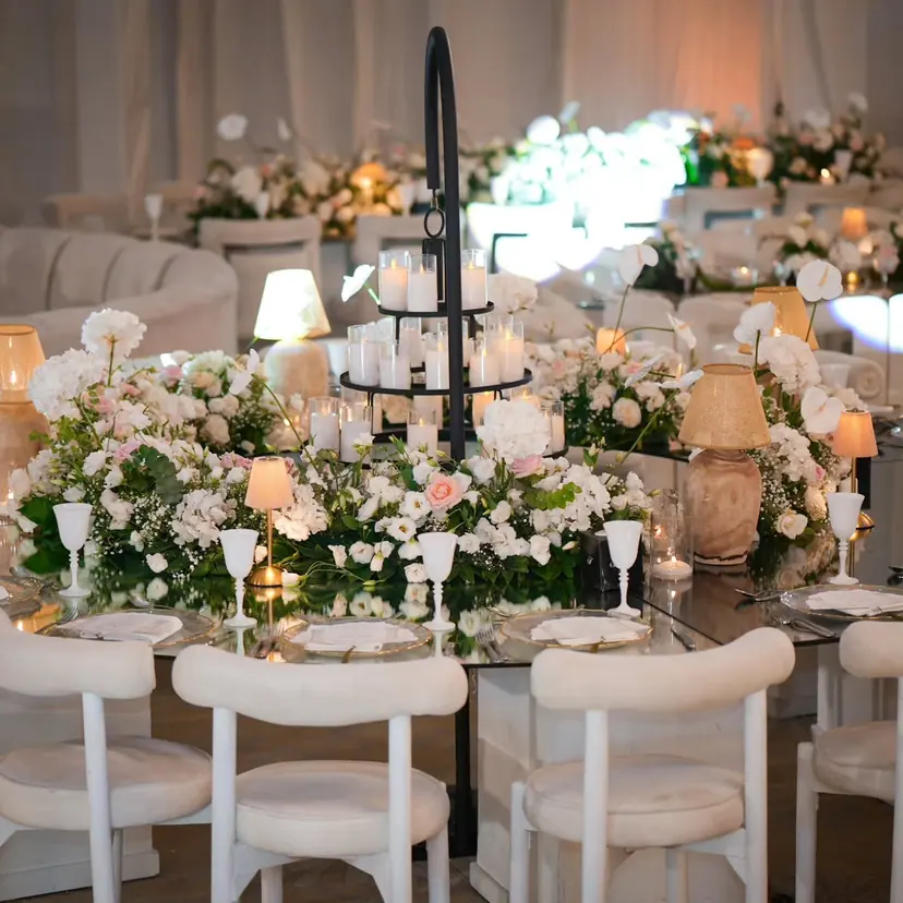 A round table with a centrepiece of white roses and hydrangeas under a black iron candle frame