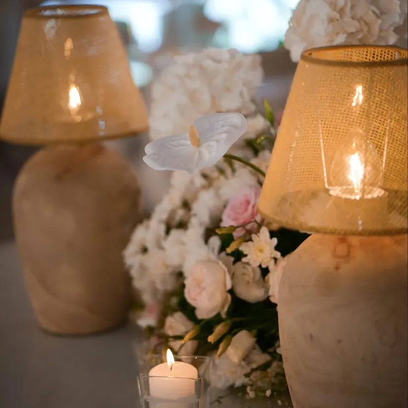 Two linen table lamps glowing beside white roses and a small candle