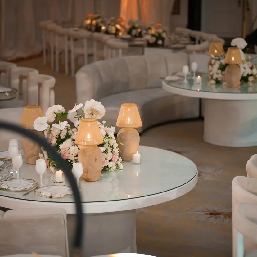 A curved cream sofa and a glass-topped table with lamps and roses