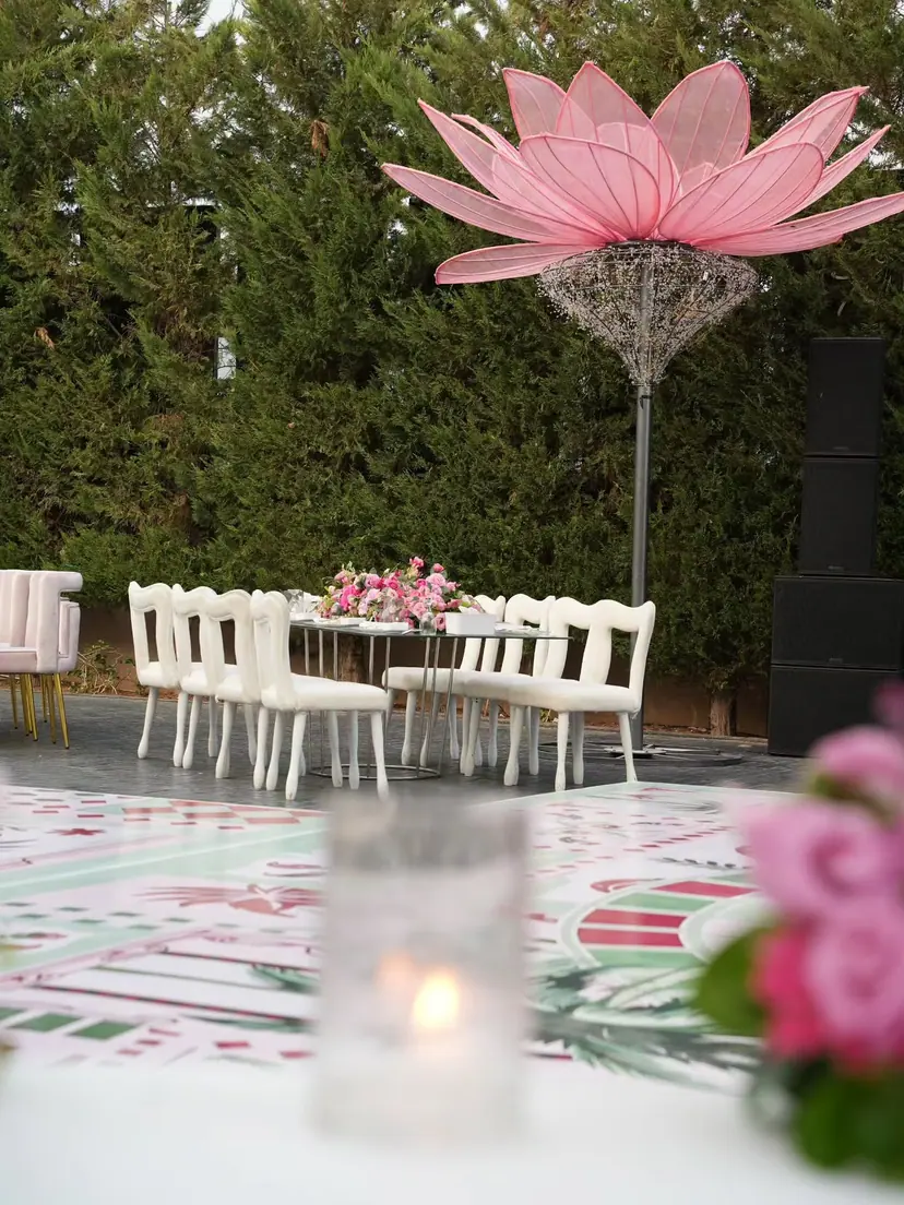 A pink lotus sculpture over white chairs, with a candle and roses on the hand-painted floor