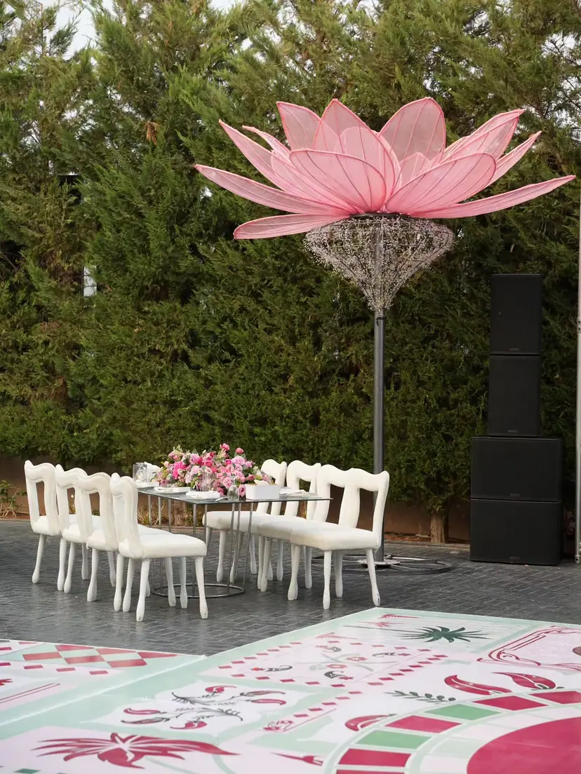 A giant pink lotus sculpture above white chairs and a table of pink flowers in a garden venue