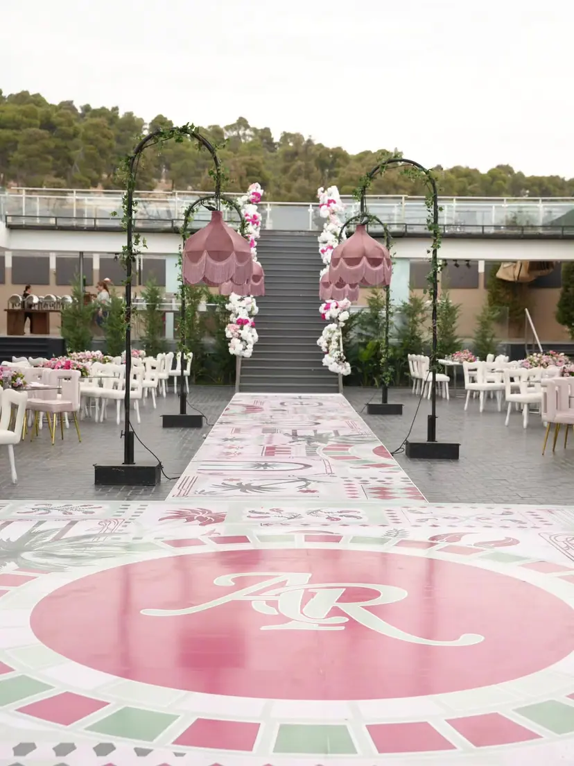 A painted aisle with the couple's monogram leading to flower arches and a staircase, outdoors