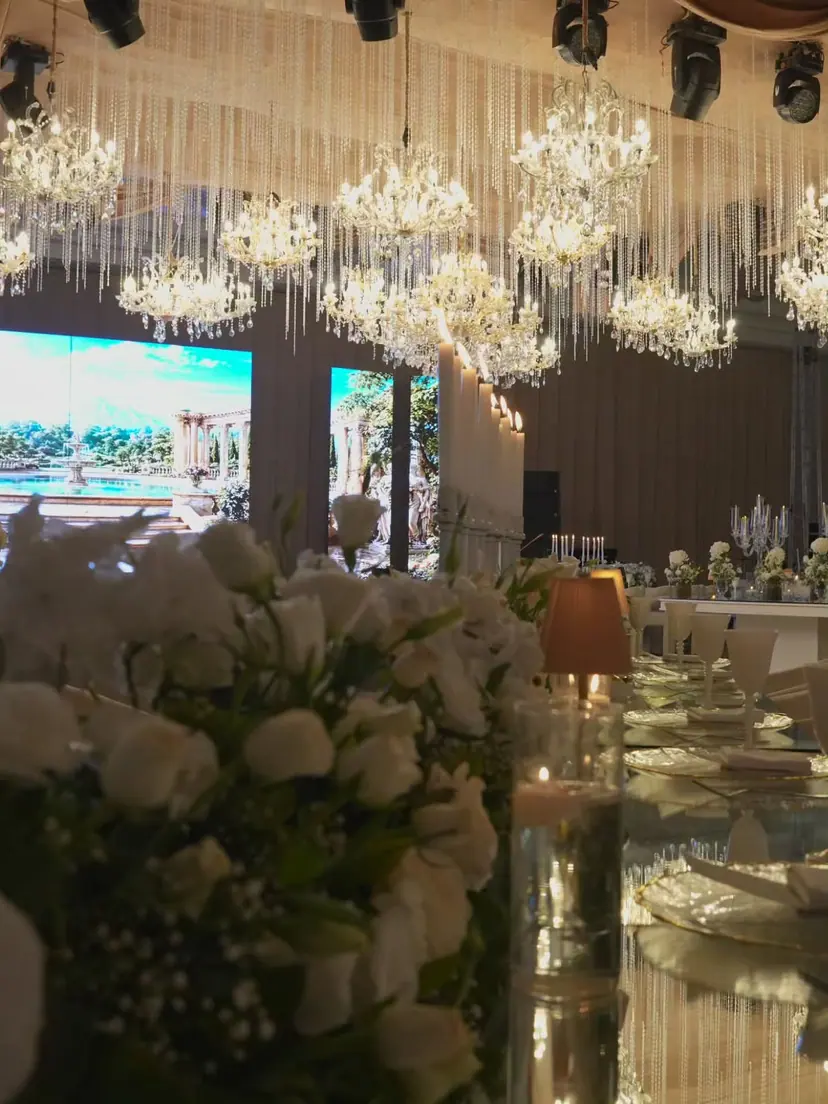 Cascading crystal chandeliers above white roses on a mirrored wedding table