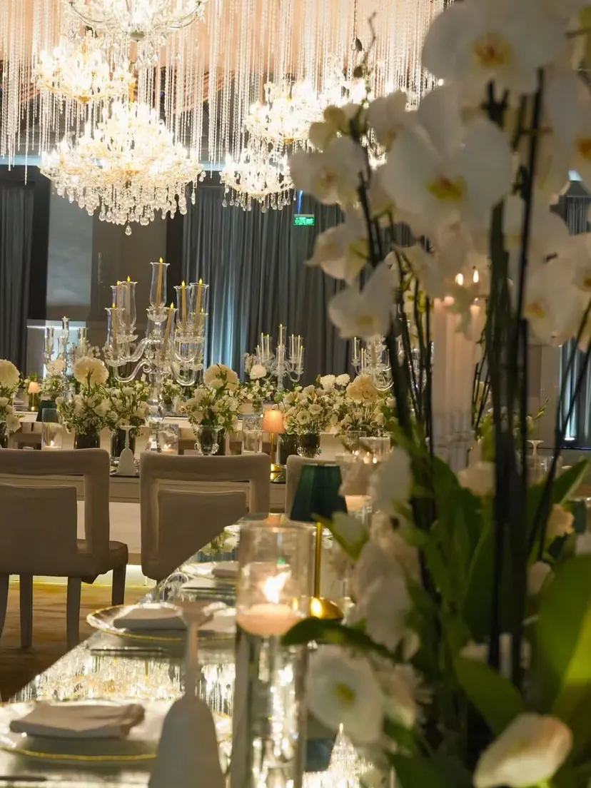 White orchids in front of a long mirrored dinner table under crystal chandeliers, set by Hyper Events at Mövenpick Amman